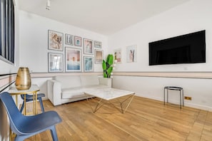 A modern living room with a white sofa, a coffee table, a TV mounted on the wall, and a series of framed pictures. - Modern Flat - 2ch/6p - Bastille (Paris)