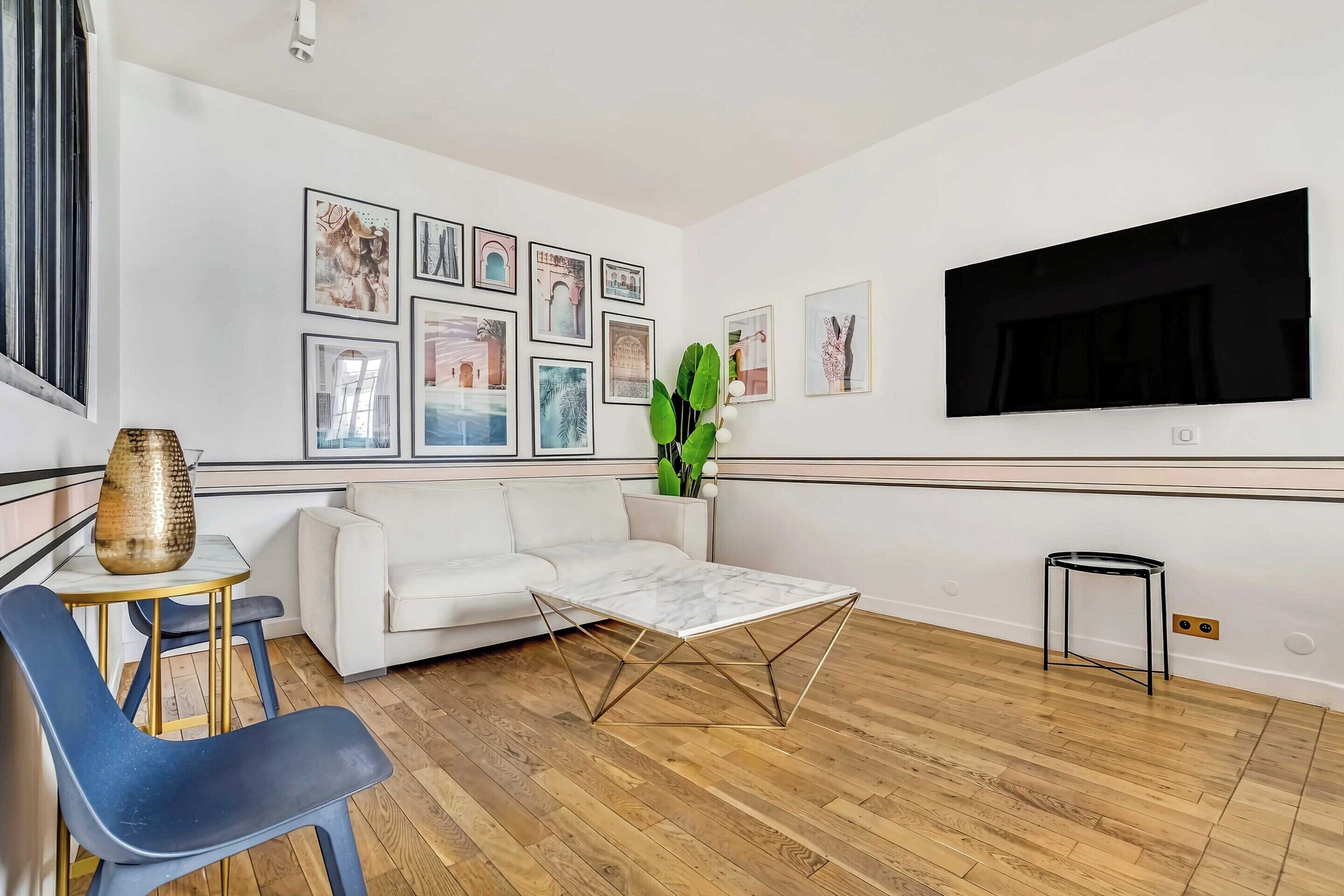 Un salon moderne avec un canapé blanc, une table basse, un téléviseur et des tableaux encadrés accrochés au mur.