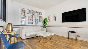 Un salon moderne avec un canapé blanc, une table basse, un téléviseur et des tableaux encadrés accrochés au mur.
