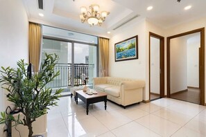 A living room with a sofa, a coffee table, a potted plant, and a painting on the wall. - Serene 2-bedroom condo with AC in Thành phố Hồ Chí Minh (Thành phố Hồ Chí Minh)