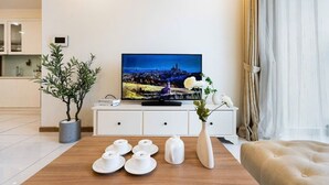 Ett modernt vardagsrum med en platt-TV, ett matbord med vita tekoppar, en vas med blommor och en soffa.