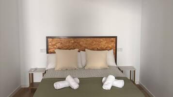 Een slaapkamer met een houten hoofdbord, twee nachtkastjes, een bed met een groene spreideken en twee opgerolde handdoeken op het bed.