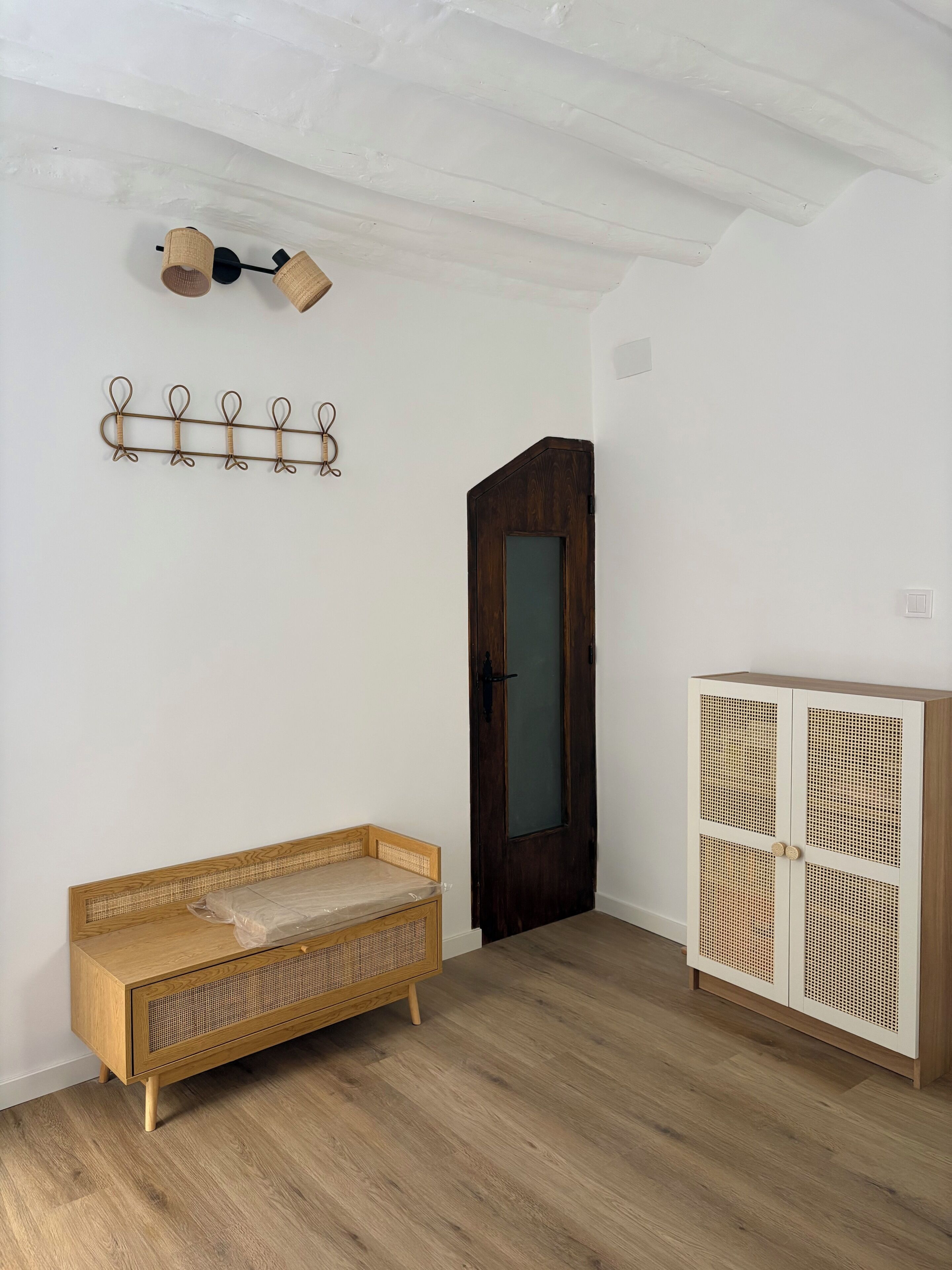 A room with a wooden bench, a cabinet with a woven design, a door, and a wall-mounted light fixture.