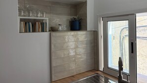 A kitchen with a built-in shelf holding glassware and a blue container.