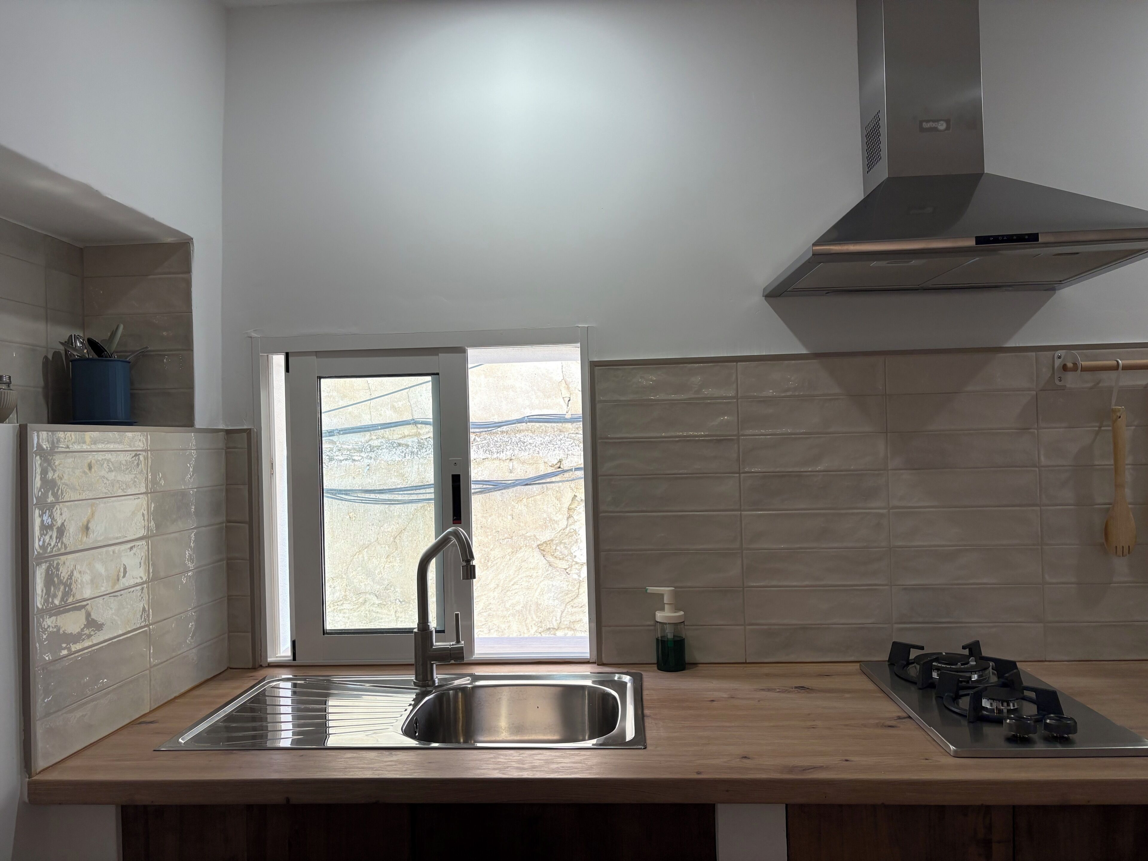 Una cocina con un lavamanos de acero inoxidable, una estufa a gas y una ventana con vistas al exterior.