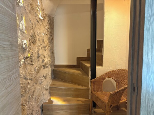 Una escalera de madera que conduce a una habitación con una silla de mimbre.