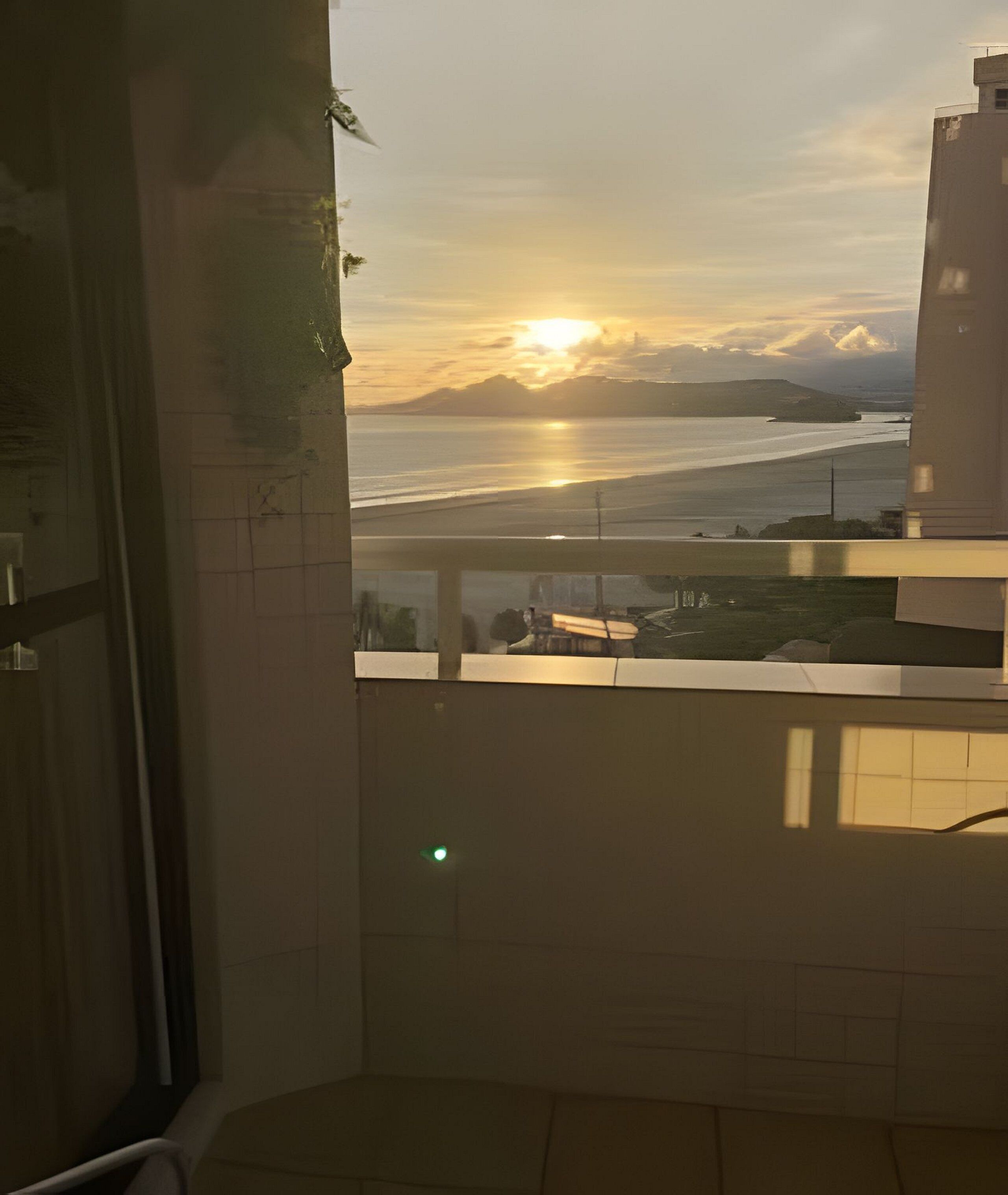 A balcony with a view of the sunset over the sea, a tiled floor, and a window with a green light.