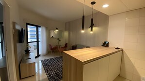 A modern kitchen with a wooden countertop, pendant lights, and a view of the living area.