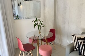 A dining area with a glass table, two red chairs, a pink ottoman, and a potted plant. - SHB Melhor prédio com vista para o mar (Santos)