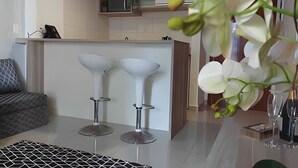A modern kitchen with two white bar stools, a grey sofa, and a decorative orchid plant.