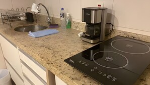 A kitchen with a granite countertop, a stainless steel sink, a coffee maker, and an induction cooktop. - SHB Melhor prédio com vista para o mar (Santos)