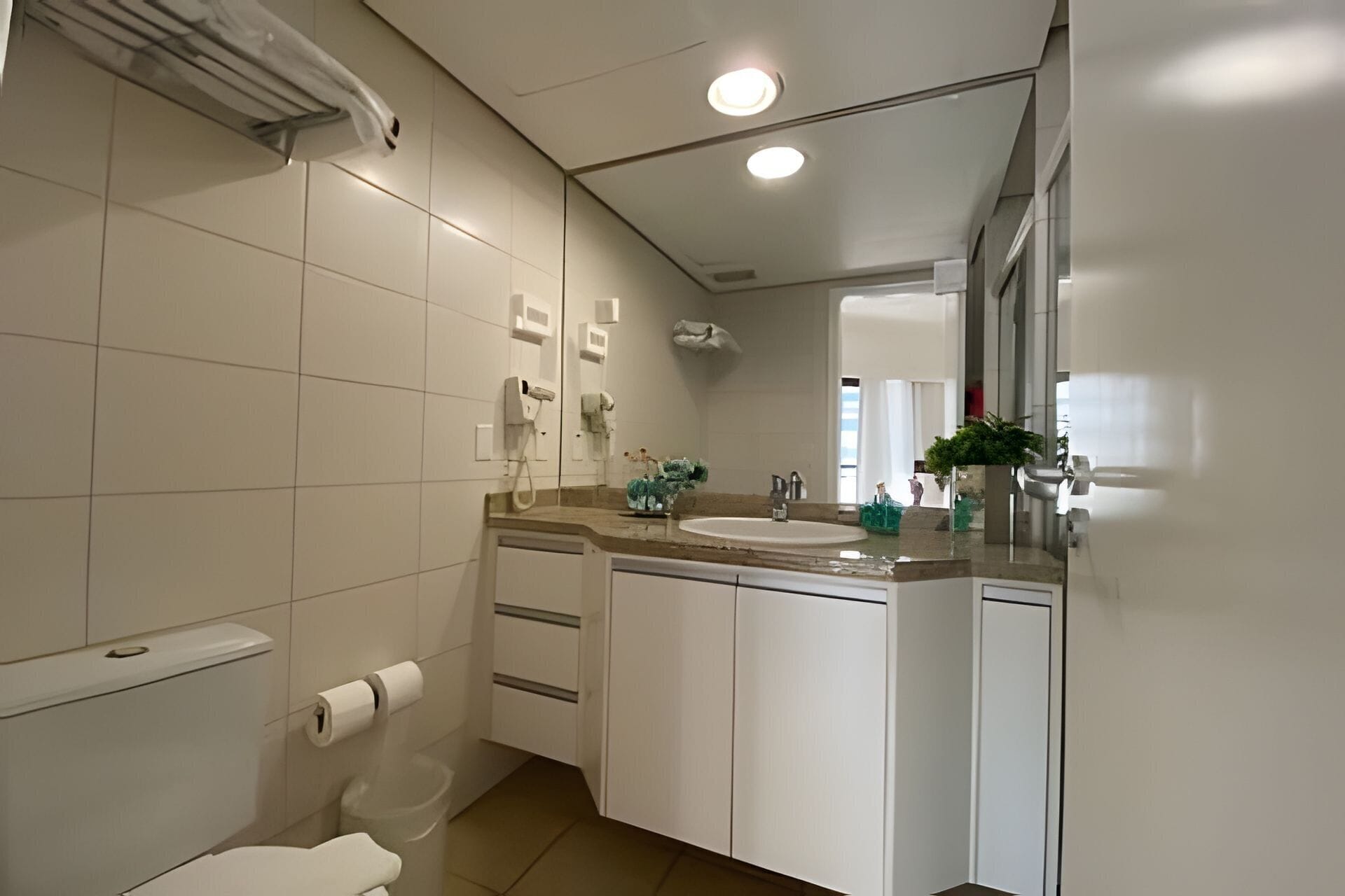 A modern bathroom with a toilet, sink, and mirror. There are white cabinets and a countertop with toiletries.