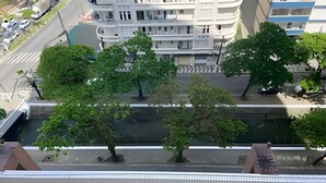 A multi-story building with balconies, a street below, and trees in the foreground.