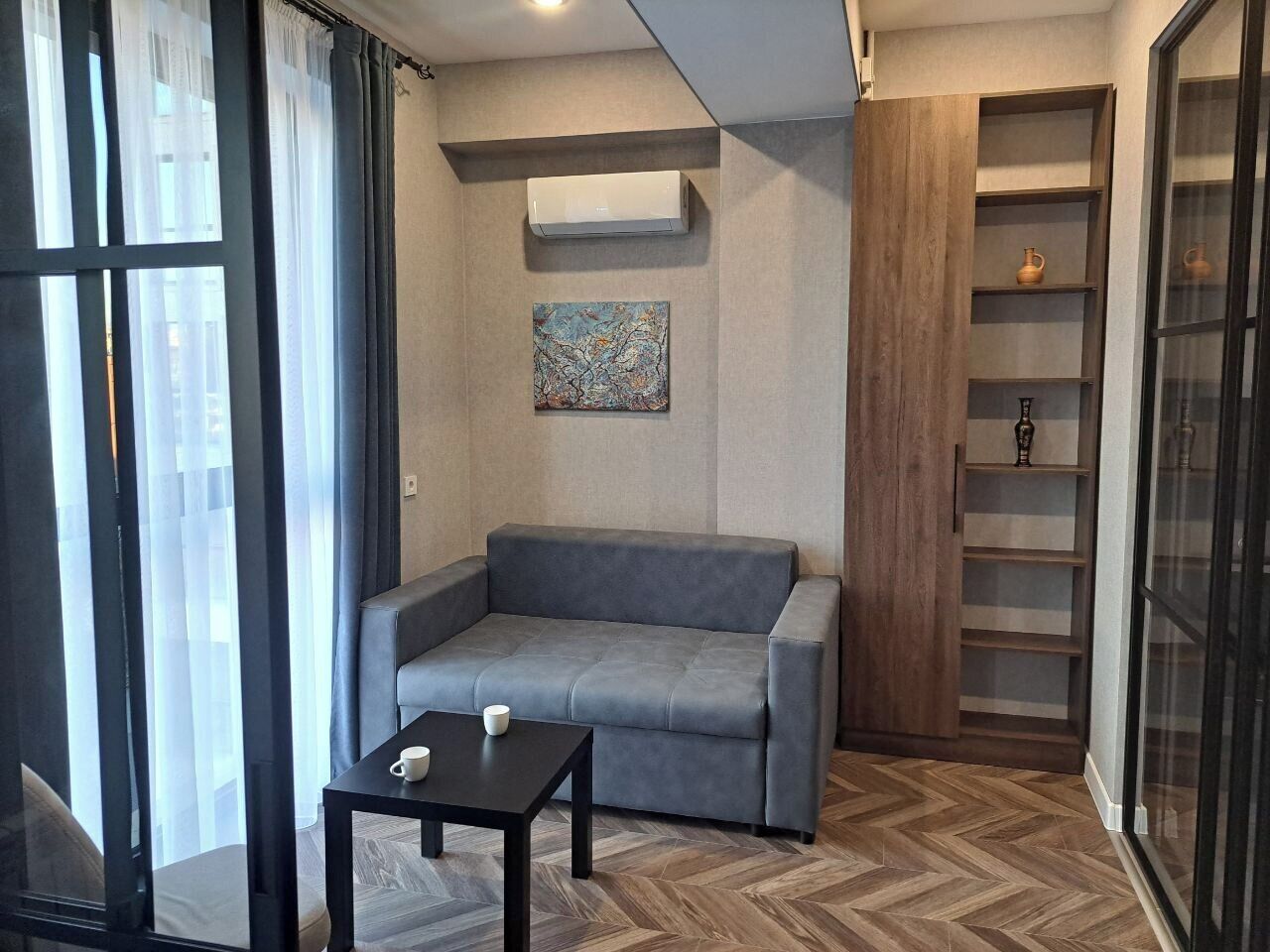 A modern living room with a grey sofa, a small table, and a wall-mounted air conditioner.
