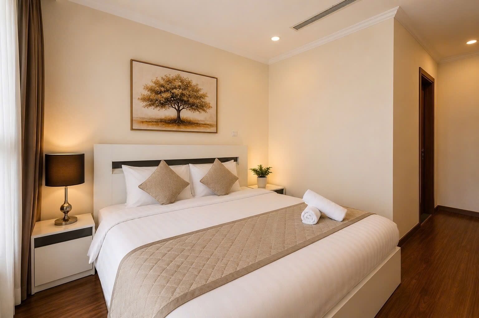 Une chambre d’hôtel avec un lit, une table de chevet avec une lampe, un tableau représentant un arbre et une plante en pot.