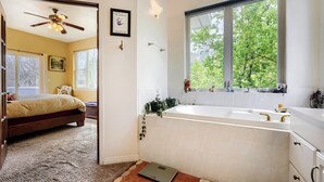 Un baño con bañera, una balanza y un ventanal con vistas a árboles.