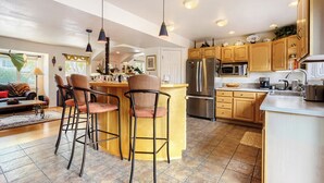 Una cocina moderna con una isla central, taburetes de bar, armarios de madera, electrodomésticos de acero inoxidable e iluminación colgante.