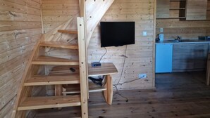 A wooden interior with a staircase, a flat-screen TV mounted on the wall, and a kitchen area with cabinets and a sink. - Holiday Home With a Terrace, Close to the Beach (Ustronie Morskie)
