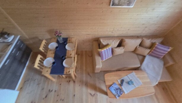 A wooden dining table with four chairs, a sofa, and a small wooden table with a cup and a menu. - Holiday Home With a Terrace, Close to the Beach (Ustronie Morskie)