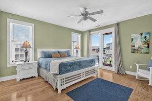 A bedroom with a bed, nightstands, a ceiling fan, and a view of the outside. - Canal Views, Saltwater Pool, Private Elevator (Carolina Beach)