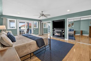 A bedroom with a bed, a TV, a fireplace, and a balcony with a view of houses. - 5BR Heated pool Oct-Nov, sunset views, near beach (Carolina Beach)