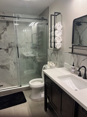 A modern bathroom with a glass shower enclosure, a toilet, a sink with a black faucet, and a mirror above the sink. - 6 ACRES RETREAT SAUNA, HOT TUB, FIRE PIT, GAMES (Jasper)