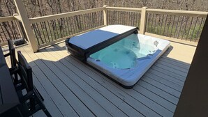 Un jacuzzi en una terraza de madera con vistas a árboles.