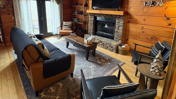Interior acogedor de una cabaña de madera con chimenea, un televisor montado encima y un cartel con la palabra 'WELCOME'.