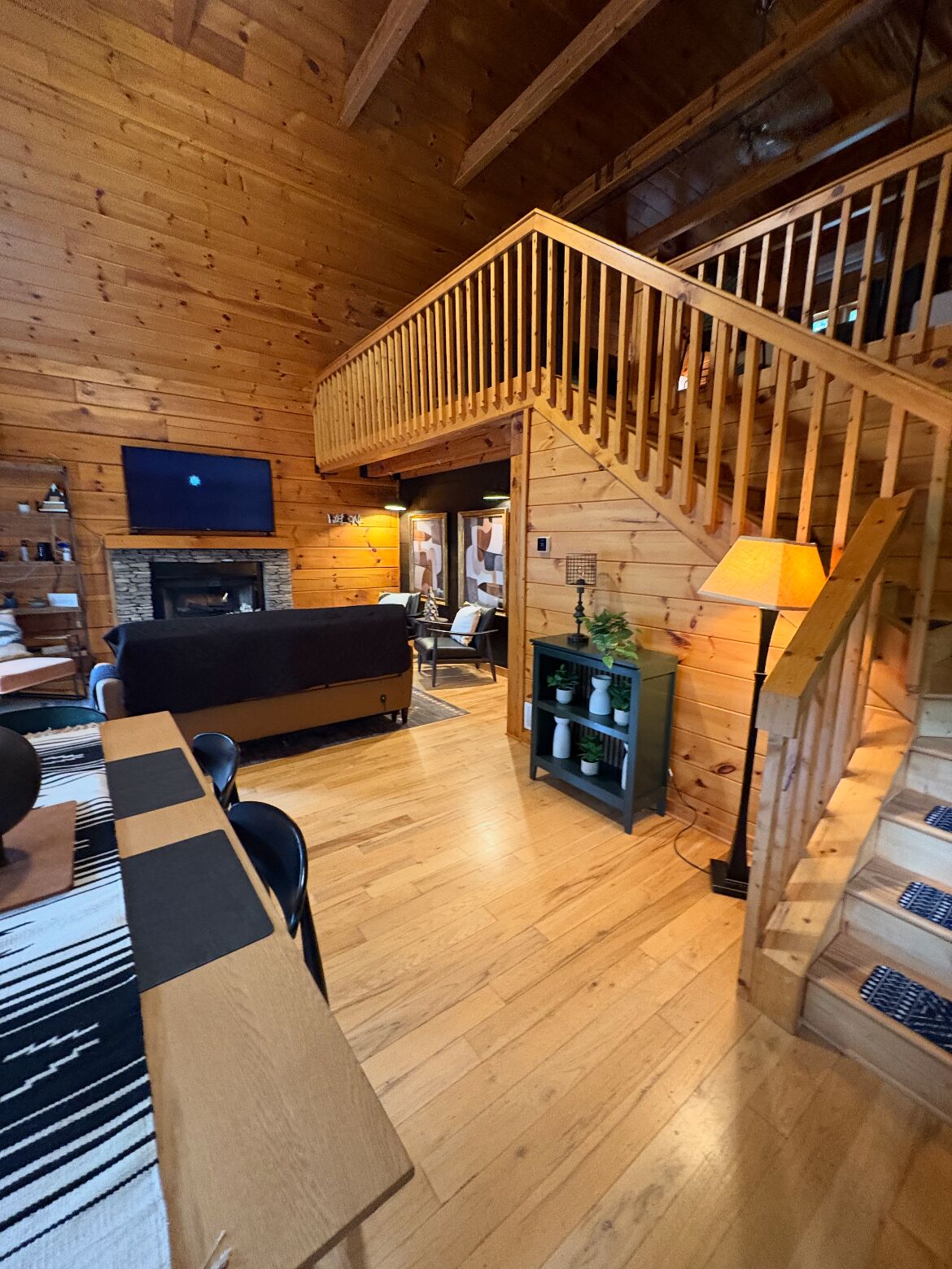 A wooden interior with a staircase, a fireplace, and a television.