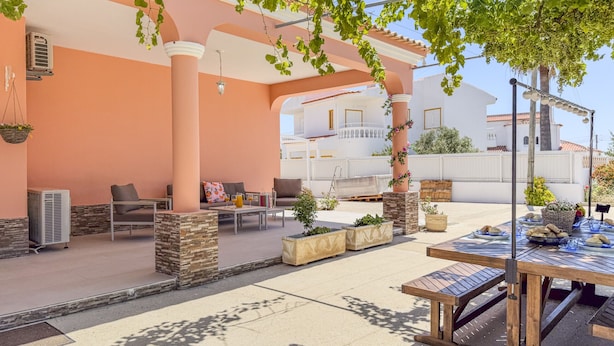 Eine Terrasse im Freien mit Sitzgelegenheiten, einem Esstisch und einer mit Wein bewachsenen Pergola.