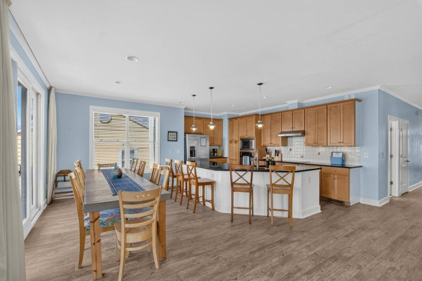 A modern kitchen with wooden cabinets, a central island, and a dining area with a long table and chairs.