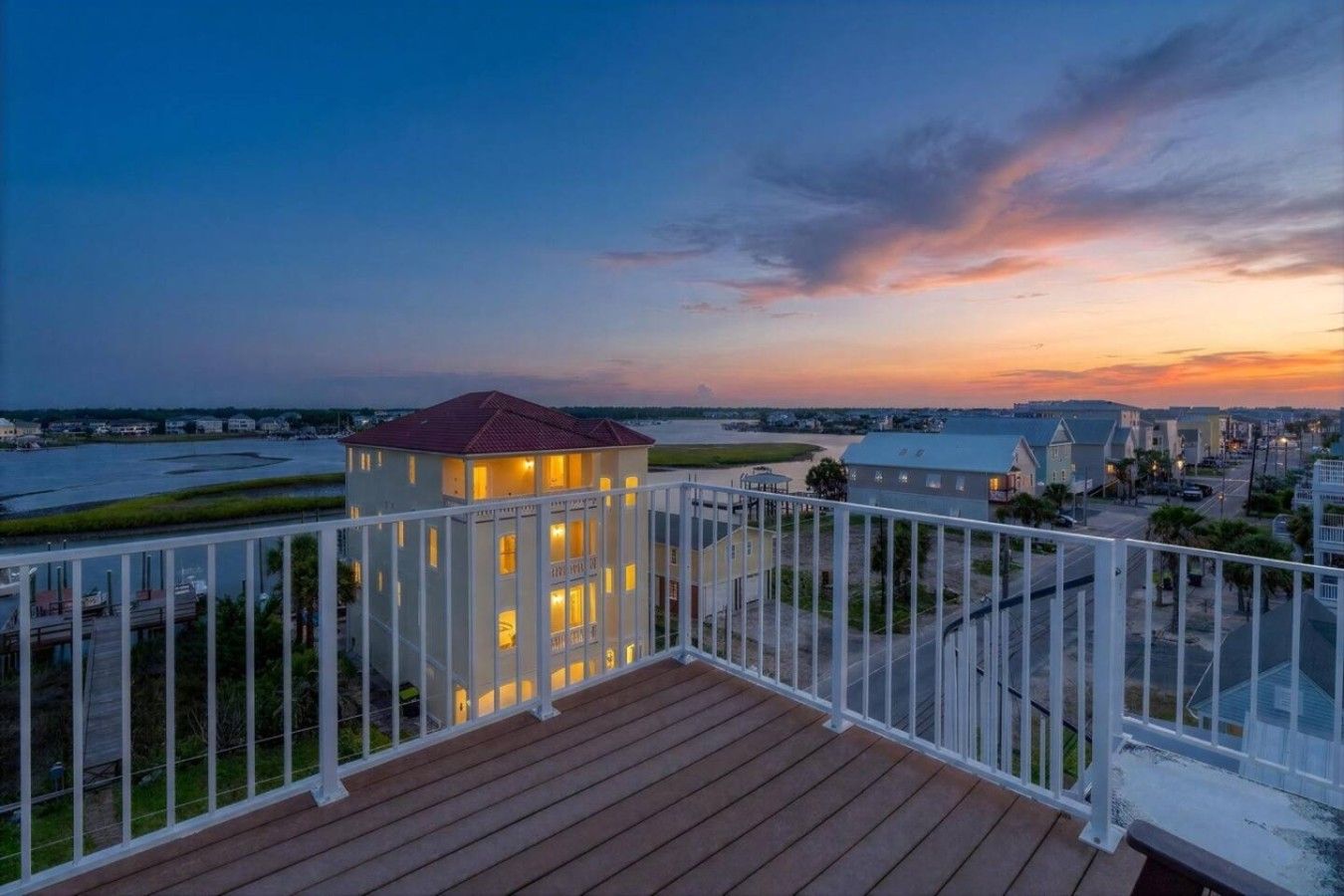 A balcony with a view of a waterfront and a small building with lights on.