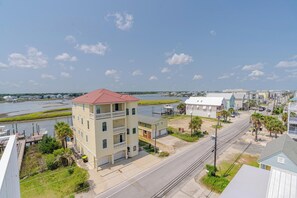 A coastal residential area with a prominent two-story building featuring a balcony, a dock, and a clear view of the water. - Canal sunset views, private saltwater pool, steps to beach (Carolina Beach)