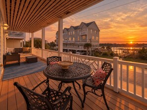 A wooden deck with outdoor furniture, a view of a residential building, and a sunset in the background. - 2 Kitchens, heated pool thru Nov, near beach (Carolina Beach)