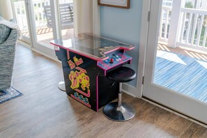 Een kamer met een tafel met glazen blad, voorzien van een spel, een zwarte stoel en uitzicht door een glazen deur op een terras.