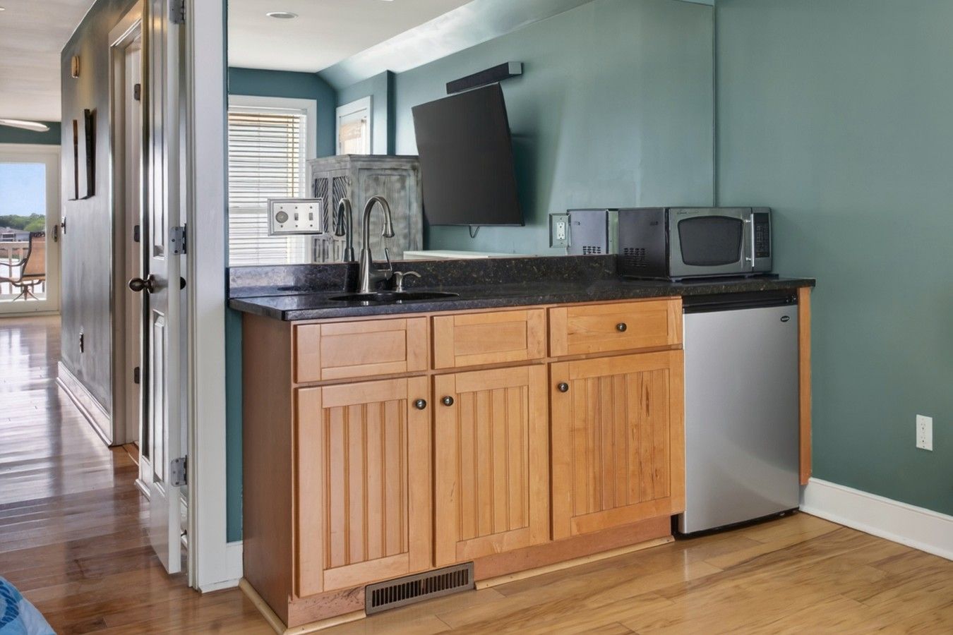 A kitchen with wooden cabinets, a stainless steel refrigerator, a microwave, and a flat-screen TV mounted on the wall.
