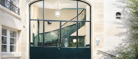 A building entrance with a large arched door, a staircase with a metal railing, and potted plants.