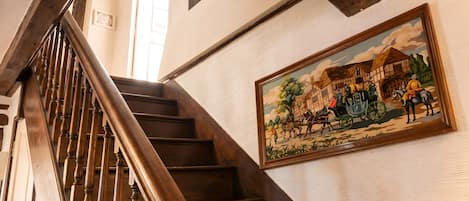 A wooden staircase with a painting of a historical scene on the wall.