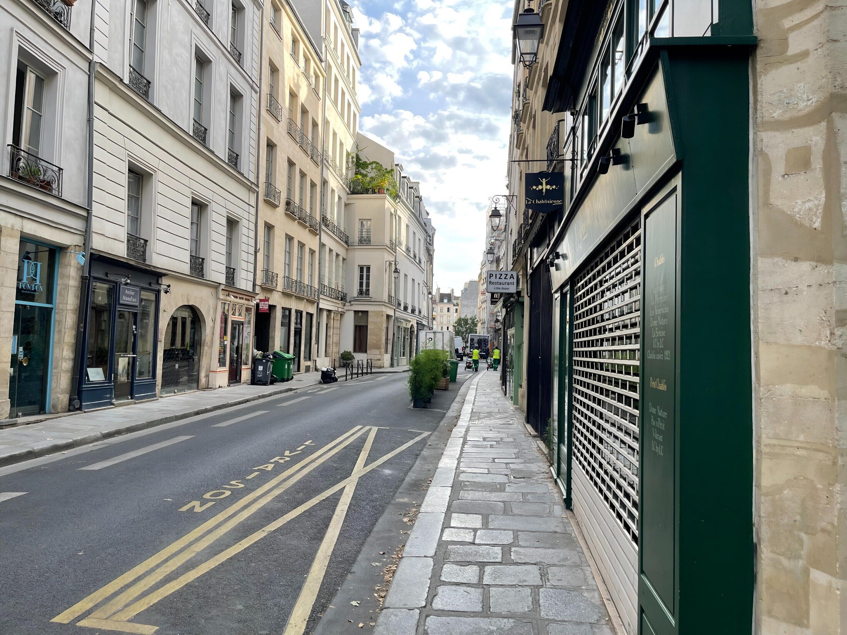 A street with buildings, a pizza restaurant sign, and a closed shutter on the right.