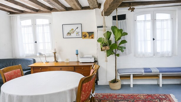 Une pièce avec une table ronde, un banc en bois, un bureau avec une imprimante et une plante suspendue.