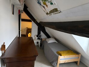 Une pièce avec un plafond en pente, un bureau en bois, un lit avec un cadre en bois et une petite table avec une lampe.