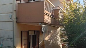 A residential building with a balcony, a gated entrance, and a tree in the background. - Cozy1-bedroom apartment, two sofa bed in enchanting peraia-neoi epivates with AC (Thessaloniki)