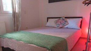 A single bed with a green blanket, a floral pillow, and a red light in the room. - Cozy1-bedroom apartment, two sofa bed in enchanting peraia-neoi epivates with AC (Thessaloniki)