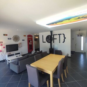 A modern living room with a sofa set, a wooden dining table, a red telephone booth, and a flat-screen TV. - House for Rent with a Private, Heated Pool in Vallon-Pont-d'Arc, Ardèche (Vallon-Pont-d'Arc)
