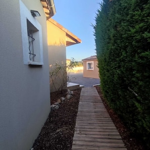 A pathway leading to a building with a small window and a security camera. - House for Rent with a Private, Heated Pool in Vallon-Pont-d'Arc, Ardèche (Vallon-Pont-d'Arc)