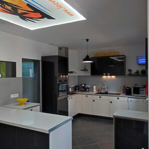 A modern kitchen with a built-in oven, a sink, and a dining area with a white countertop. - House for Rent with a Private, Heated Pool in Vallon-Pont-d'Arc, Ardèche (Vallon-Pont-d'Arc)