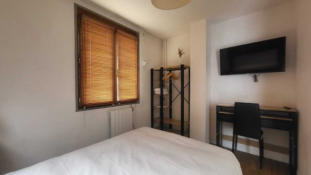 A bedroom with a bed, a desk, a chair, a radiator, and a TV mounted on the wall. - Private Room in a Local's Home (Le Trait)