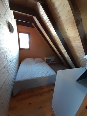 Une petite pièce avec un toit en pente, comprenant un lit simple, une petite table et une fenêtre.