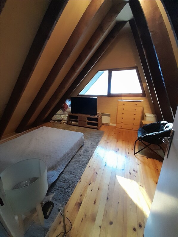 Une chambre mansardée avec un plafond en pente, un lit, une télévision, une petite commode et une fenêtre.