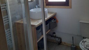 Ett badrum med en duschkabin i glas, en vit handfat, ett träfönster och en toalett med ett dekorativt lock.